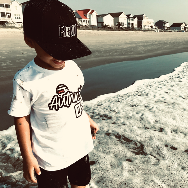 Young Boy standing at the beach shore wearing Authnik Brand Alliance Tshirt and Really Excited About Life Hat